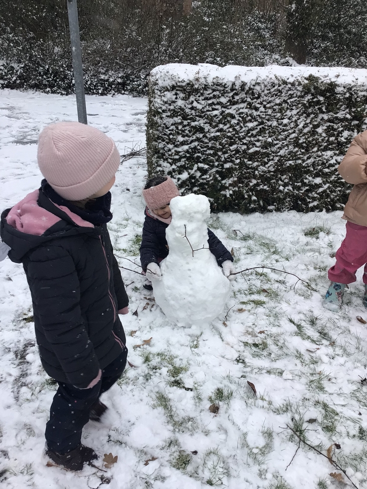 Foto dreier Kindergartenkinder im Schnee, die einen Schneemann bauen